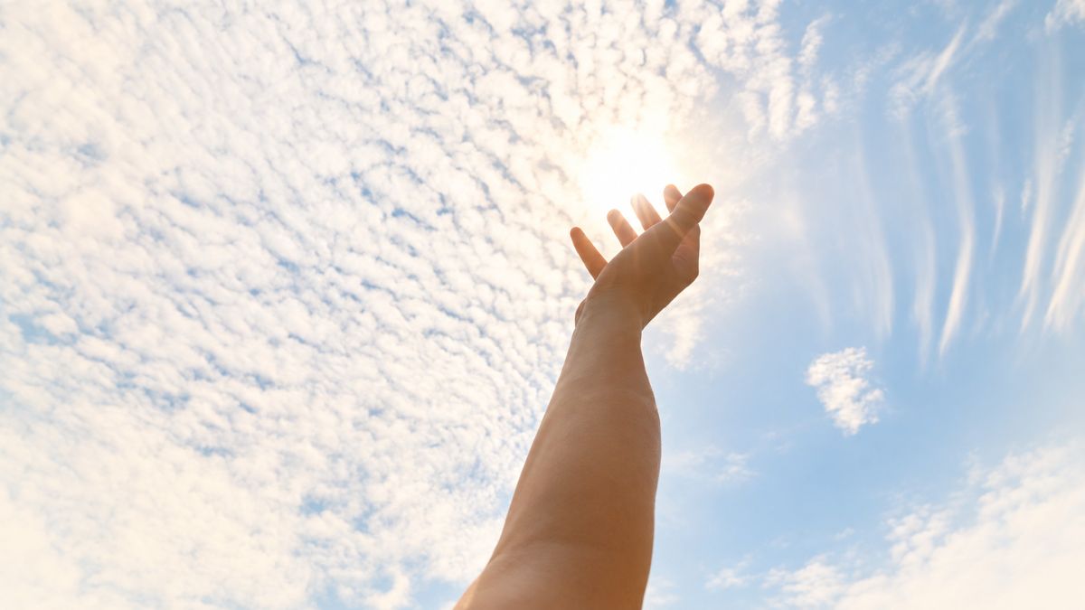 Main tendue vers le soleil à travers les nuages